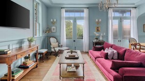 A room with a wooden coffee table, a pink sofa, a wooden side table, and a large flat-screen TV mounted on the wall.