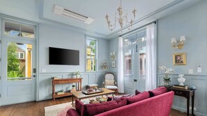A living room with a large window, a flat-screen TV, a wooden coffee table, a red sofa, and a chandelier.