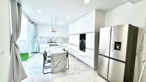 A modern kitchen with white cabinetry, a built-in oven, a stainless steel refrigerator, and a marble countertop. - The White House (Santa Lucía de Tirajana)