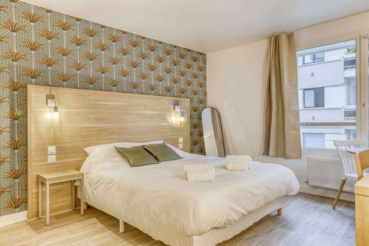 A modern hotel room with a large bed, bedside table, and a view of the city through the window.