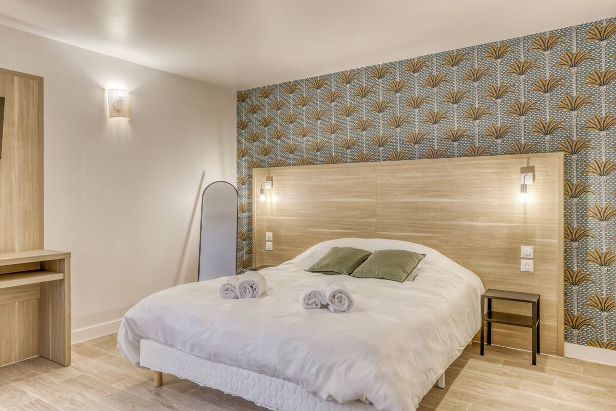 A neatly made bed with rolled towels, a wooden headboard, and a patterned wallpaper.