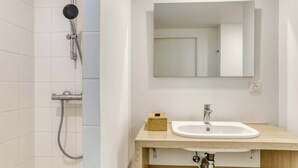 Een badkamer met een douche, wastafel, spiegel en een houten wastafelmeubel.