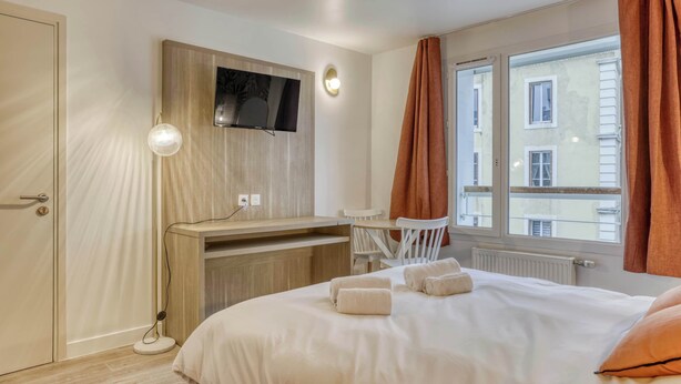 Een hotelkamer met een bed, een bureau, een stoel, een aan de muur bevestigde televisie en een raam met gordijnen.