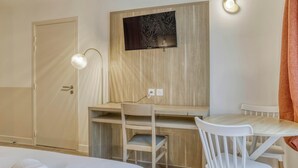 Een hotelkamer met een houten bureau, een stoel, een aan de muur bevestigde televisie en een nachtkastje met een opgerolde handdoek.
