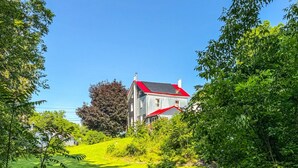 A two-story house with a red roof and white walls, surrounded by lush greenery and trees. - Elk Creek Farmhouse near Penn State! (Millheim)