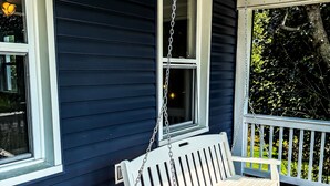 A porch with a white swing bench, dark blue siding, and a white railing. - Elk Creek Farmhouse near Penn State! (Millheim)