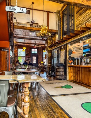 L’intérieur d’un restaurant avec un plancher en bois, des tables, des chaises, un bar et un panneau indiquant « Main St. ».