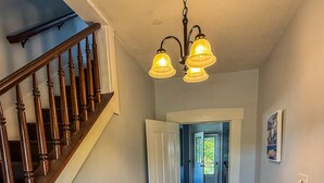 A wooden staircase with a bench, a hallway with wooden flooring, and a ceiling light fixture. - Elk Creek Farmhouse near Penn State! (Millheim)