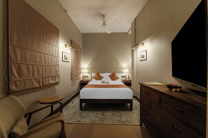 A hotel room with a large bed, bedside tables with lamps, a TV, a wooden dresser, and a chair.