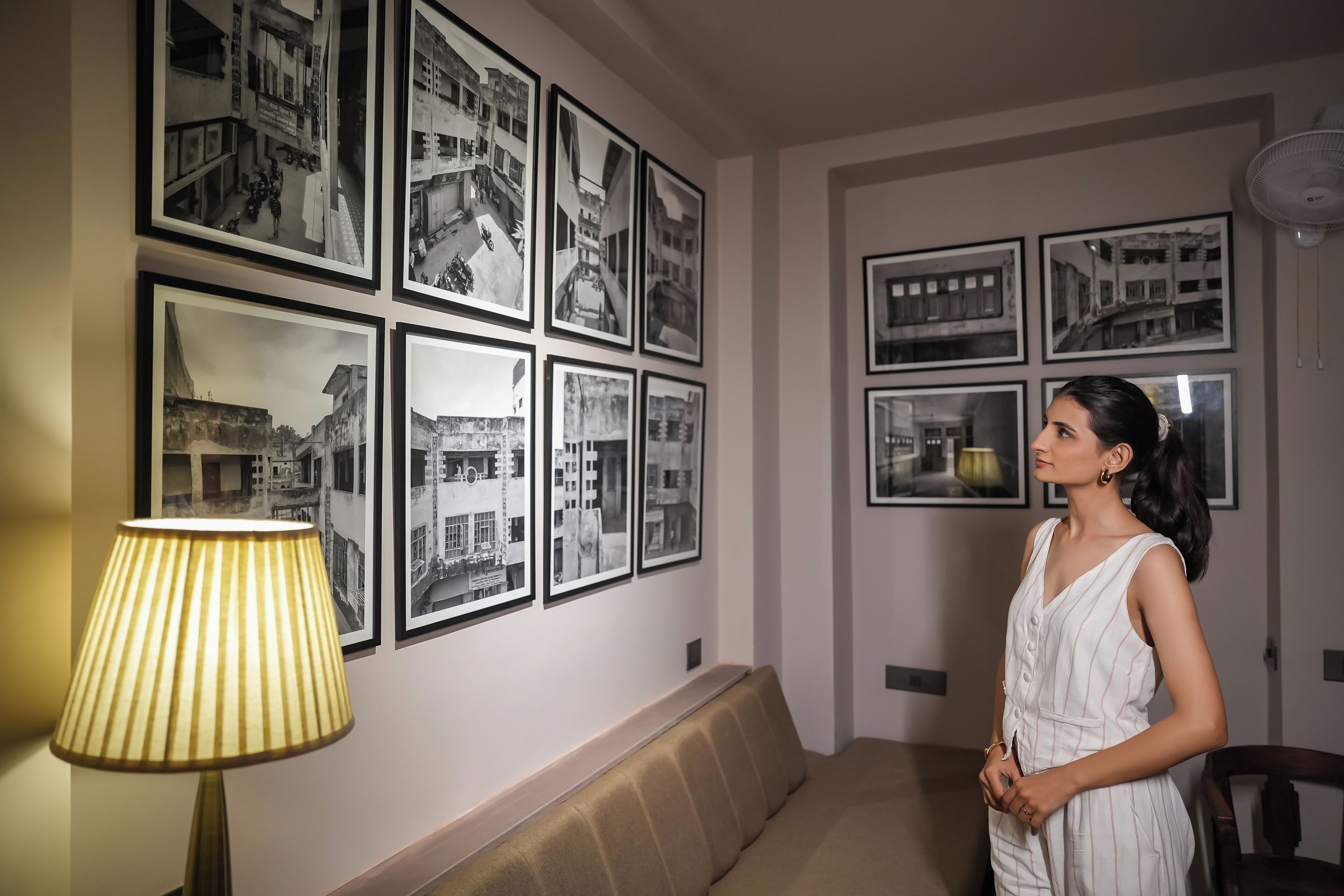 A room with a sofa, a lamp, and multiple framed photographs on the wall.