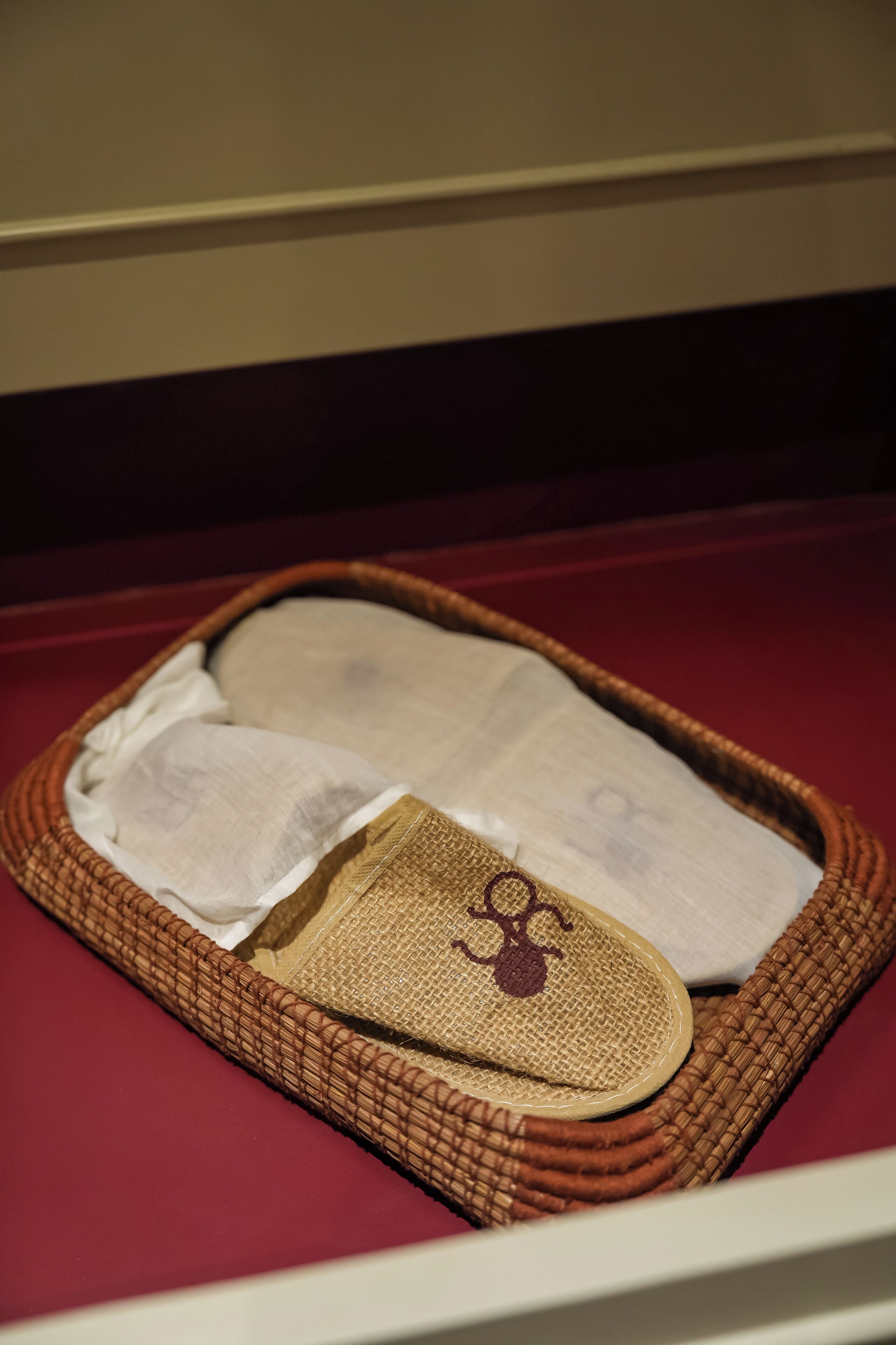 A wicker basket with a white cloth and a brown cloth on a red surface.