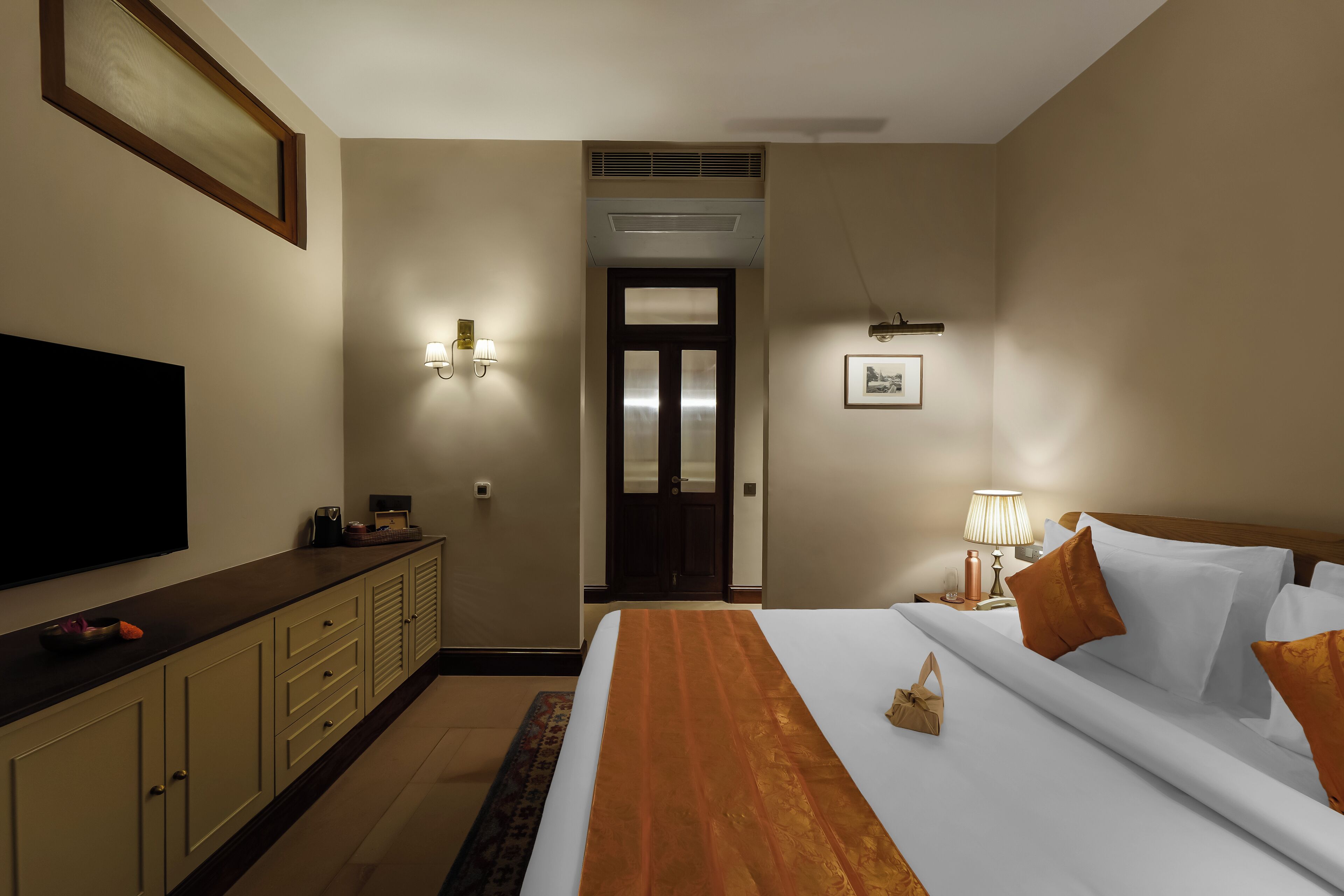 Une chambre d’hôtel avec un lit, une table de chevet, une lampe et un téléviseur fixé au mur.