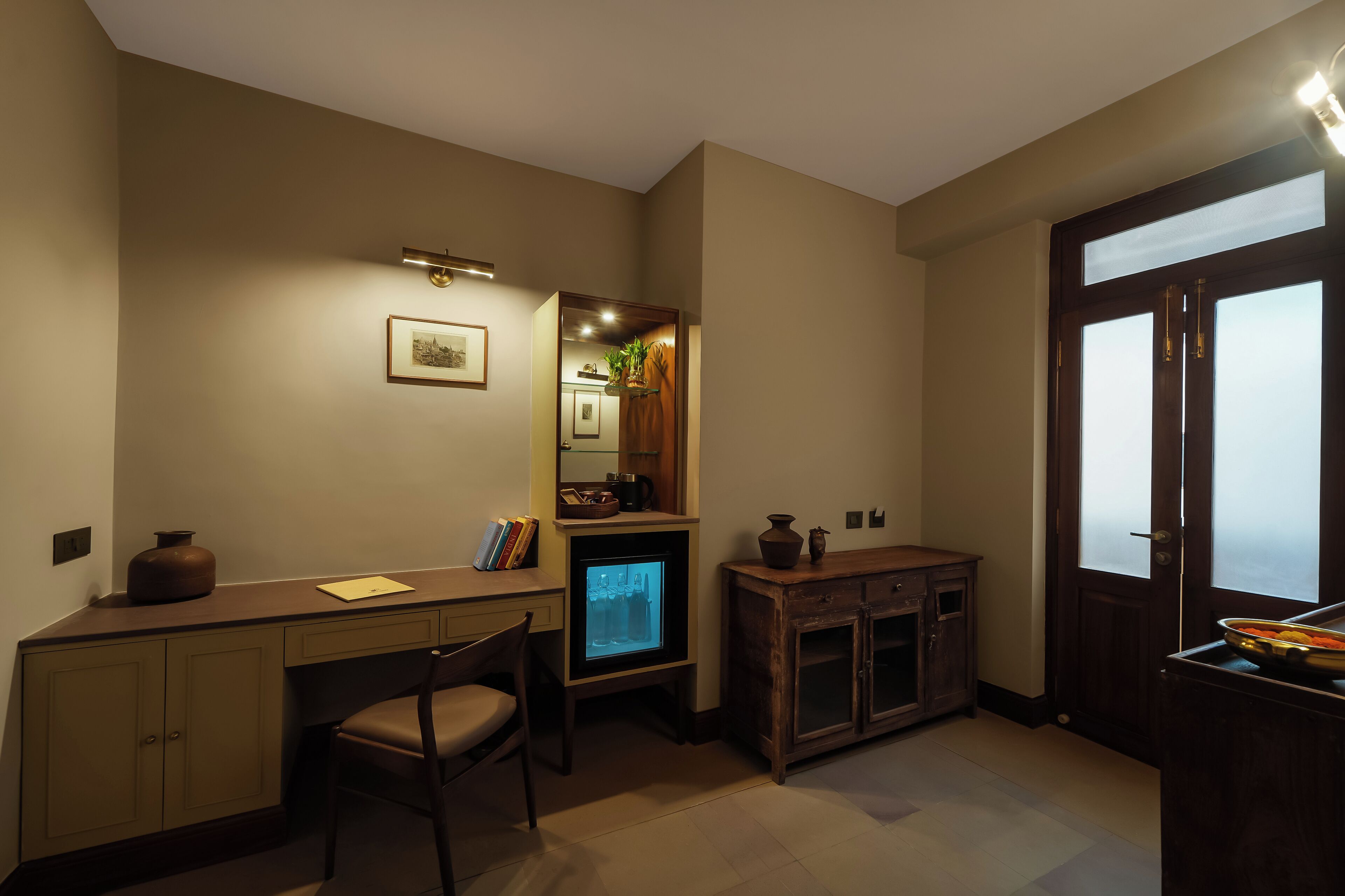 Quarto compacto e bem iluminado, com escrivaninha, cadeira e um pequeno armário.