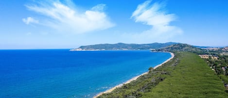 A coastal landscape with a beach, greenery, and distant hills.