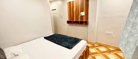 A small, modern bedroom with a bed, a wooden cabinet, and a patterned floor.