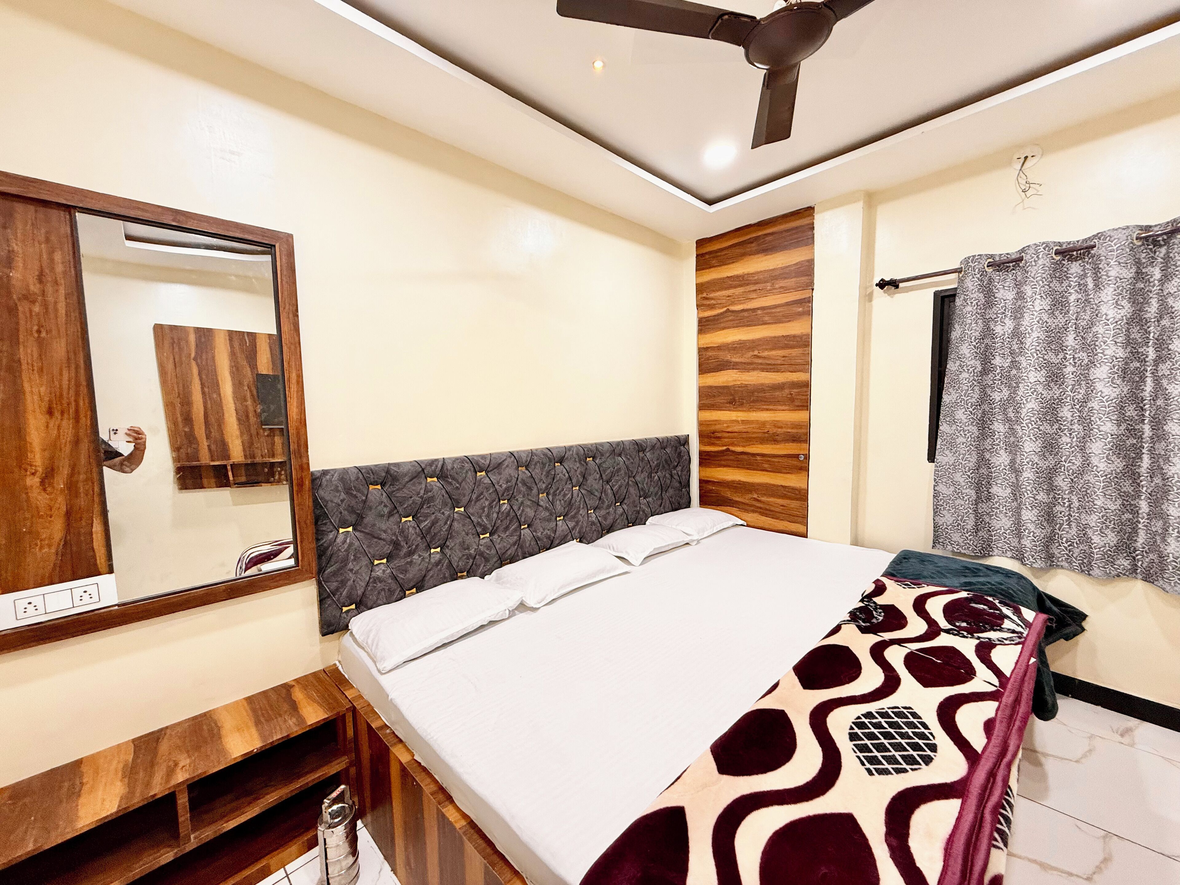 A bedroom with a bed, a ceiling fan, a mirror, and a wooden panel wall.