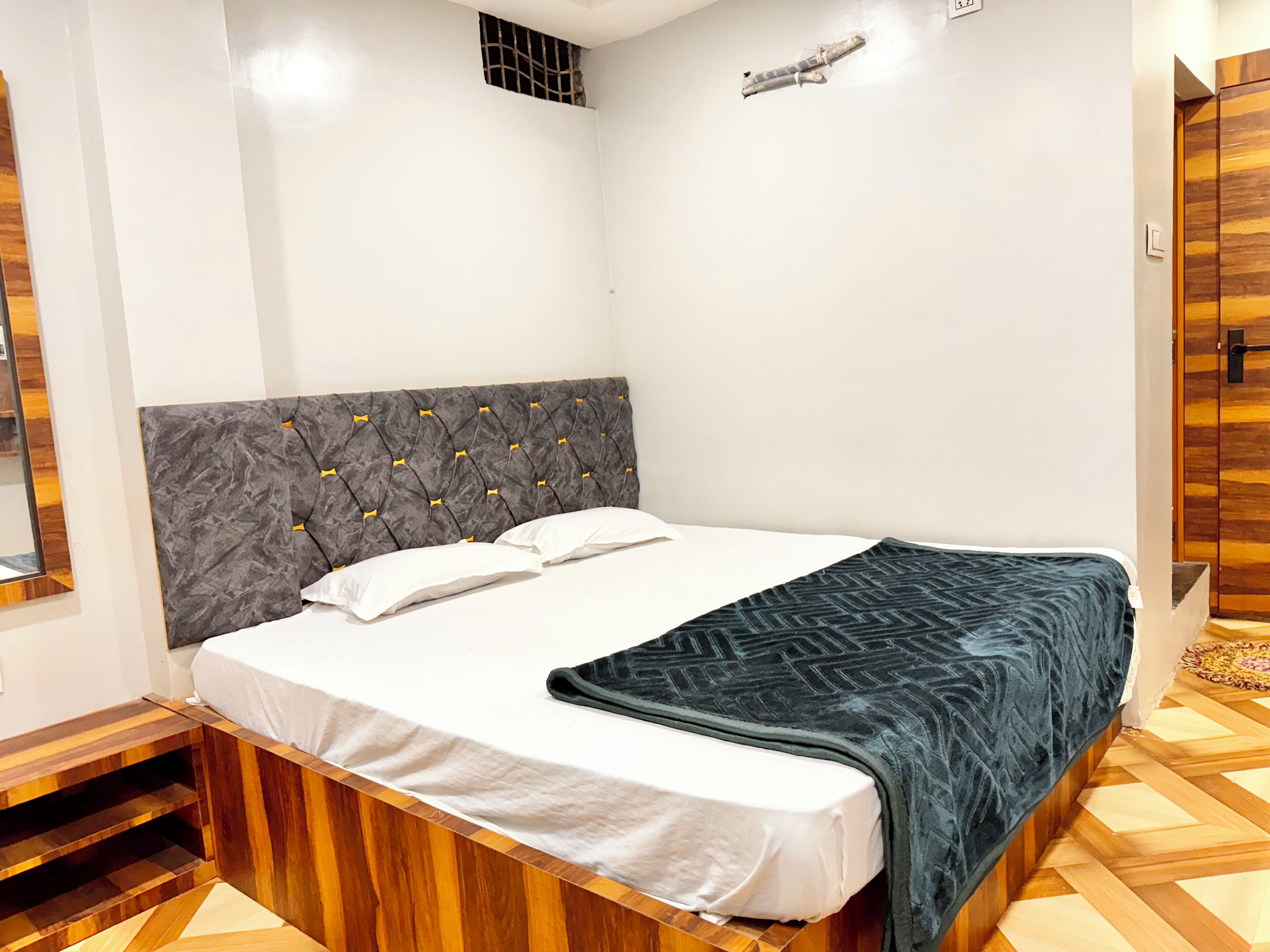 A bedroom with a wooden bed frame, a grey upholstered headboard, white bedding, and a dark blue blanket.