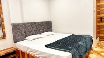 Quarto com estrutura de cama de madeira, cabeceira estofada cinza, roupa de cama branca e manta azul escura.
