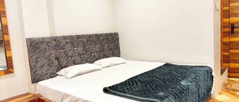 A bedroom with a wooden bed frame, a grey upholstered headboard, white bedding, and a dark blue blanket.