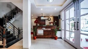 A reception area with a wooden desk, potted plants, a staircase, and a large window with a view of the outside.