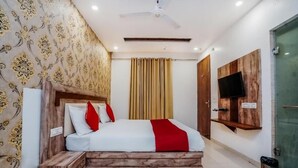 A bedroom with a bed, wooden headboard, curtains, a mounted TV, and a ceiling fan.