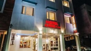 A hotel with a modern facade, a prominent red sign, and a well-lit entrance.