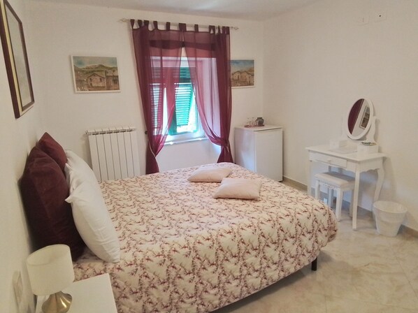 Un dormitorio con una cama, un escritorio pequeño, un radiador y una ventana con cortinas.