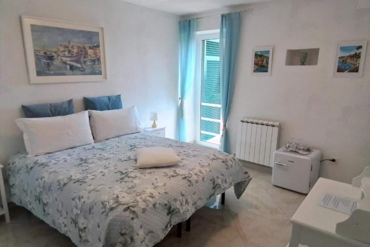 A bedroom with a bed, a nightstand, a radiator, and a desk with a chair.