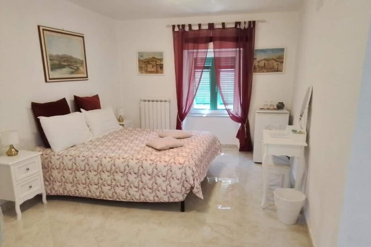 A bedroom with a bed, bedside tables, a desk, and a window with curtains.