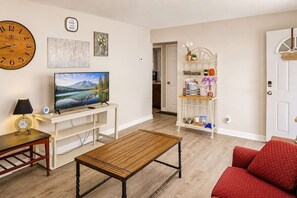A living room with a television, a clock, a coffee table, a sofa, and a bookshelf.