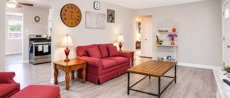 En stue med en rød sofa, et træ sofabord og et ur på væggen.