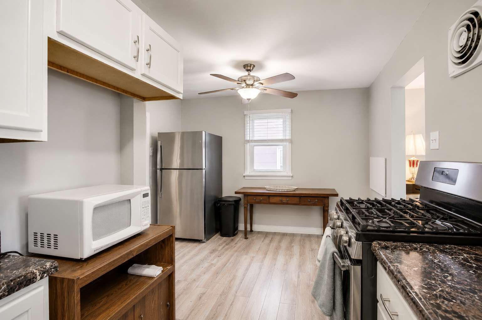A compact kitchen with a stainless steel refrigerator, a microwave, a gas stove, and a ceiling fan.