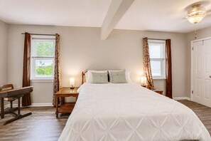 A bedroom with a large bed, two bedside tables with lamps, a wooden chair, and a door.