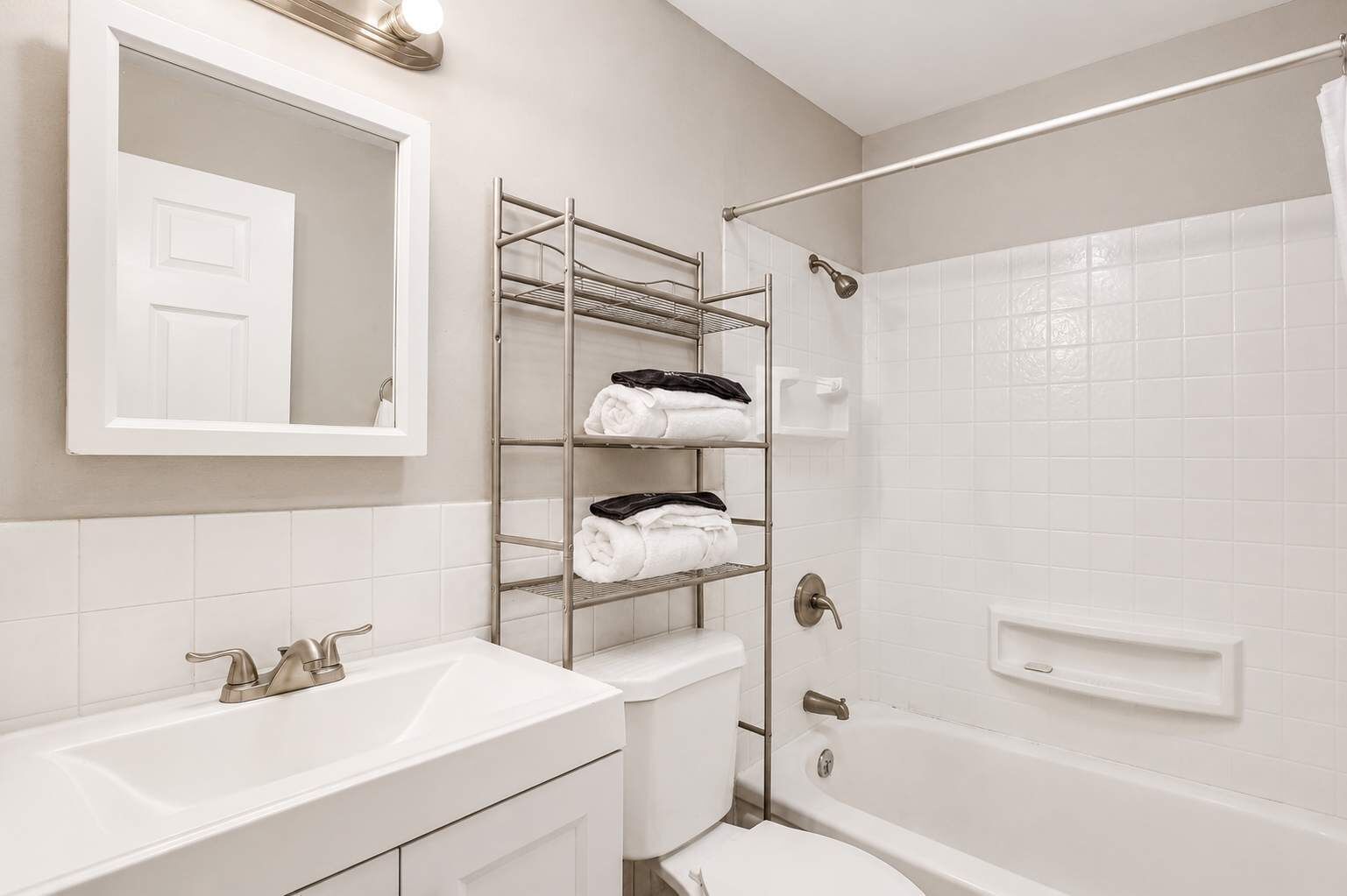 Une salle de bain avec un lavabo blanc, un miroir, un porte-serviettes, une douche et des toilettes.