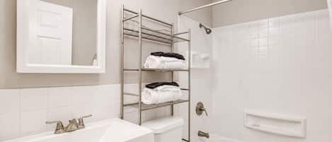 Un baño con lavamanos blanco, un espejo, toallero, ducha e inodoro.