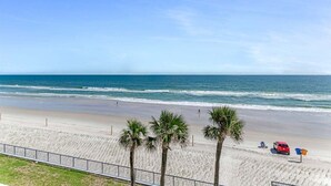 A beach with a clear view of the ocean, a sandy shore, and a few palm trees. - Wavecrest Waters at the Ashley (Daytona Beach)
