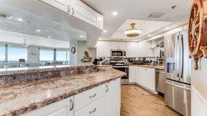 A modern kitchen with white cabinets, granite countertops, stainless steel appliances, and a large island. - Wavecrest Waters at the Ashley (Daytona Beach)