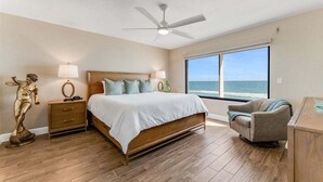 A bedroom with a bed, nightstands, a statue, a chair, and a large window with a view of the ocean. - Wavecrest Waters at the Ashley (Daytona Beach)