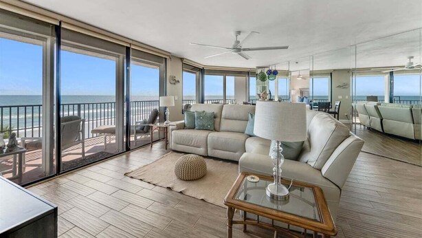 A spacious living area with a large window overlooking the ocean, a ceiling fan, and a comfortable seating arrangement. - Wavecrest Waters at the Ashley (Daytona Beach)