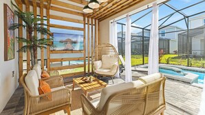 Una habitación soleada con muebles de mimbre, una silla colgante y vistas a una piscina.