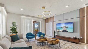 Una sala de estar moderna con un sofá, dos sillones, una mesa de centro y un televisor en la pared.