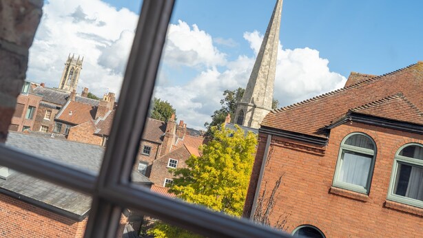A view through a window of a brick building with a prominent tower and a tree with yellow leaves. - Clifford St - Apartment 8 - sleeps 4 guests  in 2 bedrooms (York)