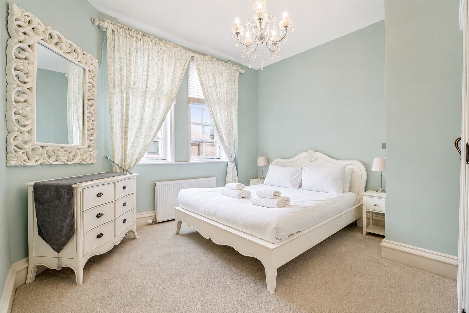 A bedroom with a bed, dresser, mirror, and chandelier.