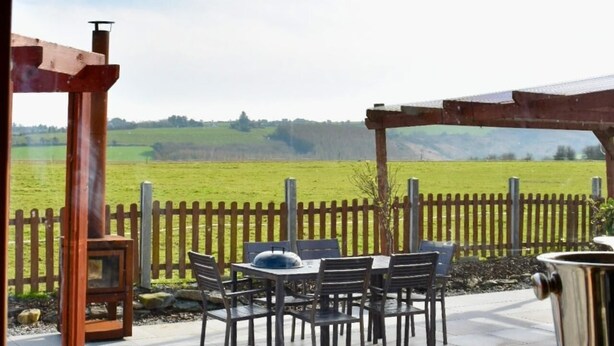 An outdoor patio with a wooden pergola, a table with chairs, and a view of a green field. - Ballinadee Bus - Boutique Bus Accommodation (Ballinadee)