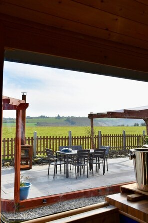 Un patio al aire libre con una pérgola de madera, una mesa con sillas y vistas a un campo verde.