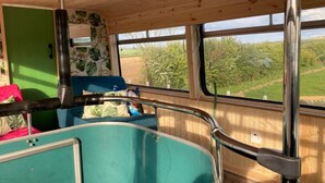 A cozy interior with a teal-colored seating area, wooden walls, and large windows offering a view of greenery outside. - Ballinadee Bus - Boutique Bus Accommodation (Ballinadee)