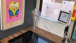 A bus interior with emergency exit signs, a no children under 16 sign, a colorful artwork, and a glass vase with pens. - Ballinadee Bus - Boutique Bus Accommodation (Ballinadee)