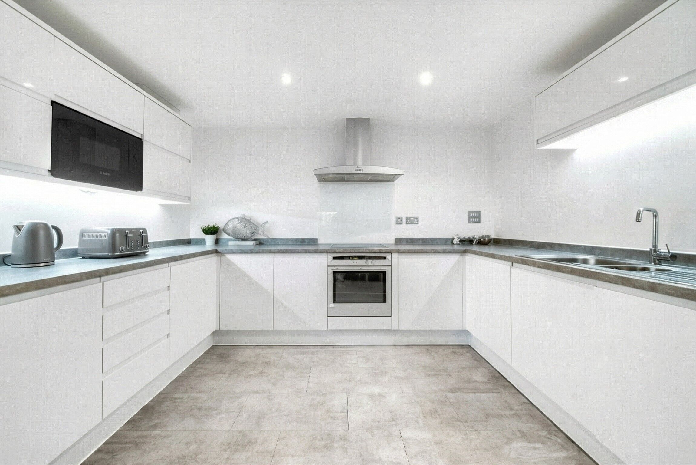 Una cocina moderna con armarios blancos, horno empotrado, microondas y pileta de acero inoxidable.