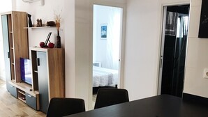 Een moderne keuken met een zwart inductiekookplaatje, houten kastjes en een ingebouwde oven. Er is een zithoek met een zwarte tafel en stoelen, en een keukeneiland met een spoelbak.