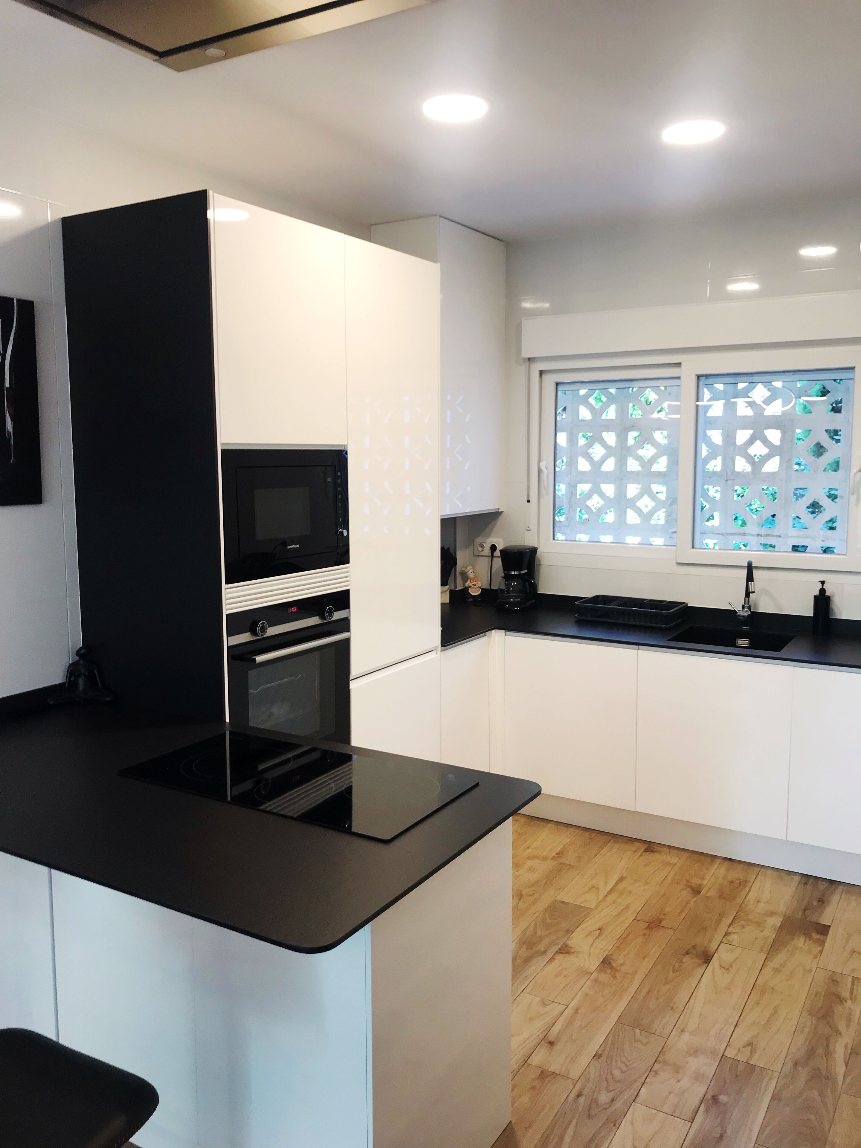 A modern kitchen with white cabinets, a black countertop, a built-in oven, and a microwave.